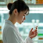 白衣を着た化粧品科学者が、ラボで試験管やビーカーを扱いながら、真剣な表情で研究に没頭している様子。創造性と精密さを表現するポートレート。